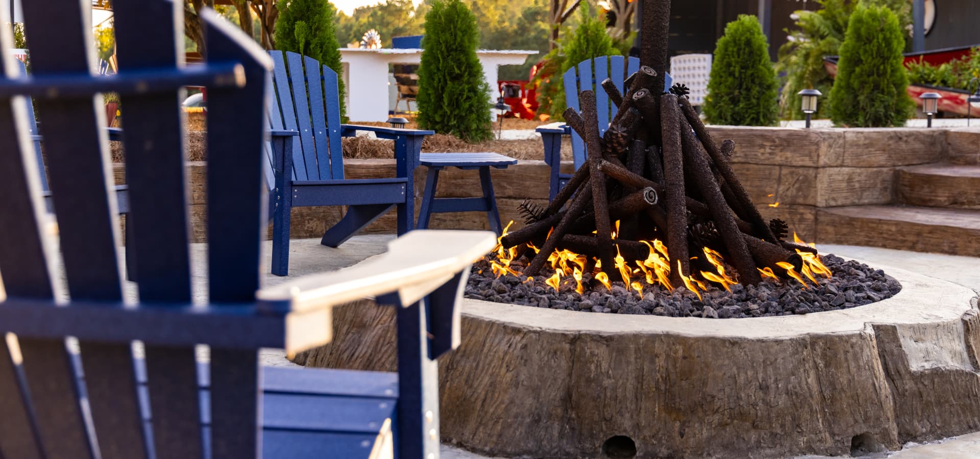 A cozy outdoor fire pit surrounded by blue adirondack chairs.