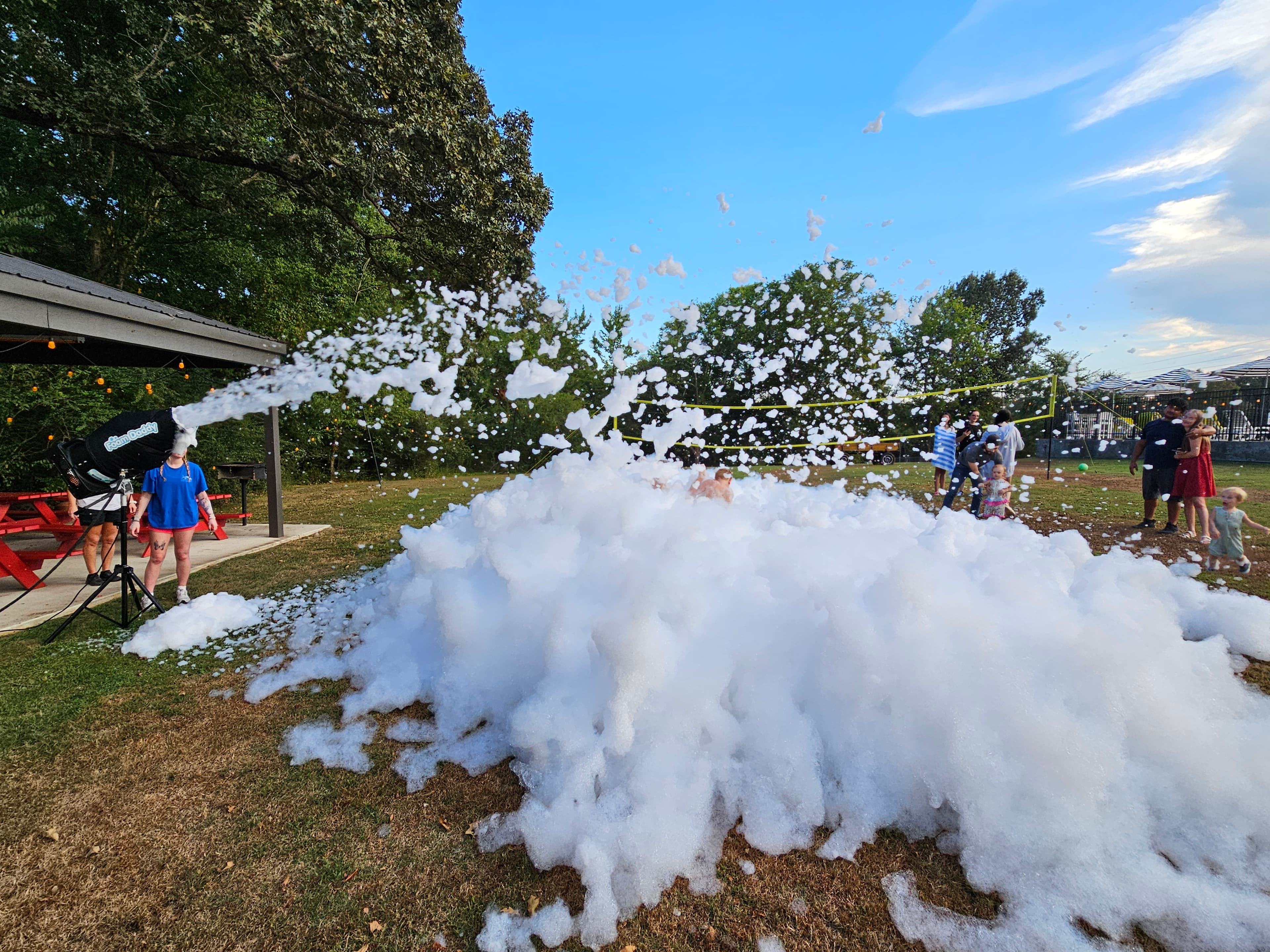 A foam machine creates a large cloud of bubbles at an outdoor gathering.