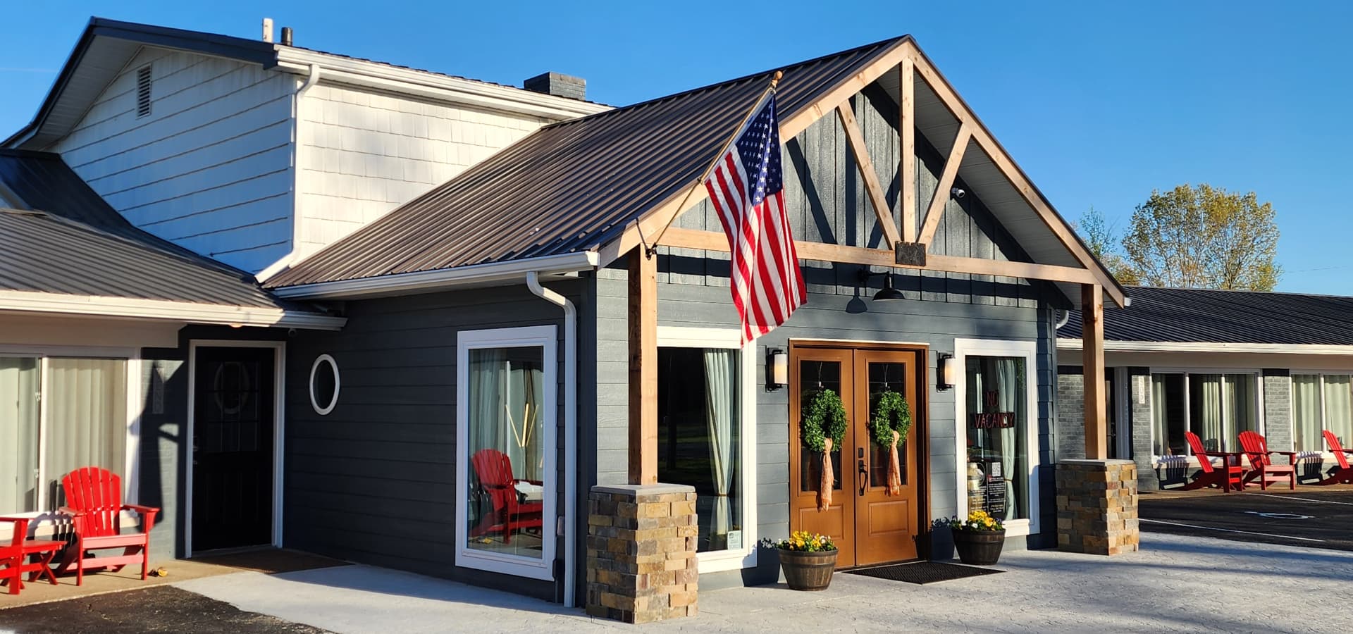 A modern building with a wooden entrance, American flag, and red chairs outside.