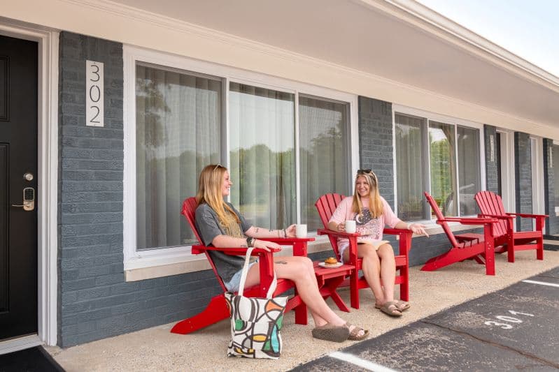 models in red adirondack chair by an exterior motel door